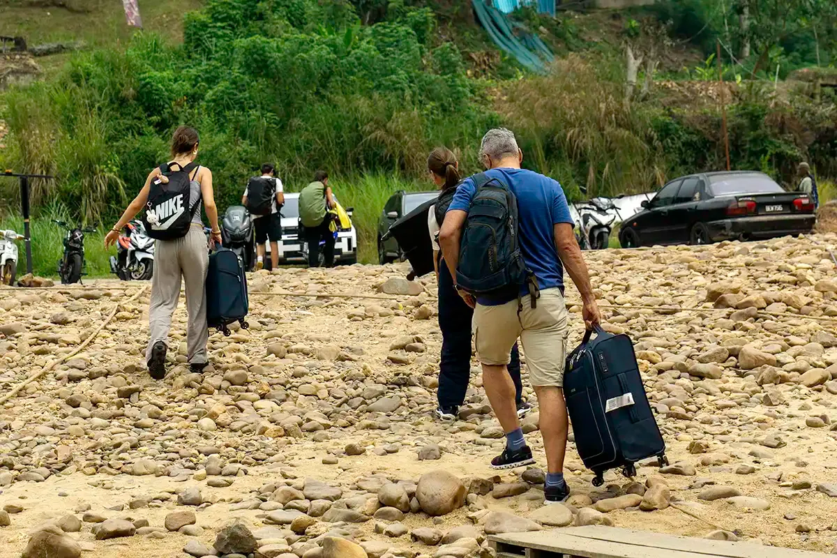 Travellers carrying luggage near the Kuala Tahan riverside after arriving in Taman Negara.