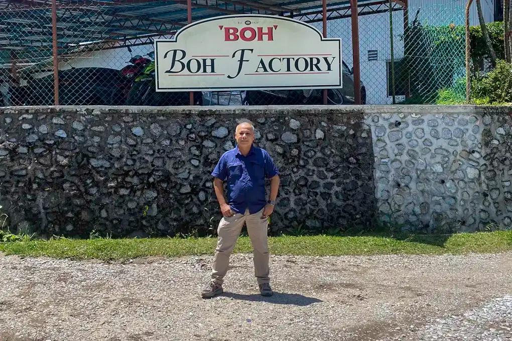 Anuar standing beside the BOH Factory sign at Habu BOH Tea Plantation in Cameron Highlands.