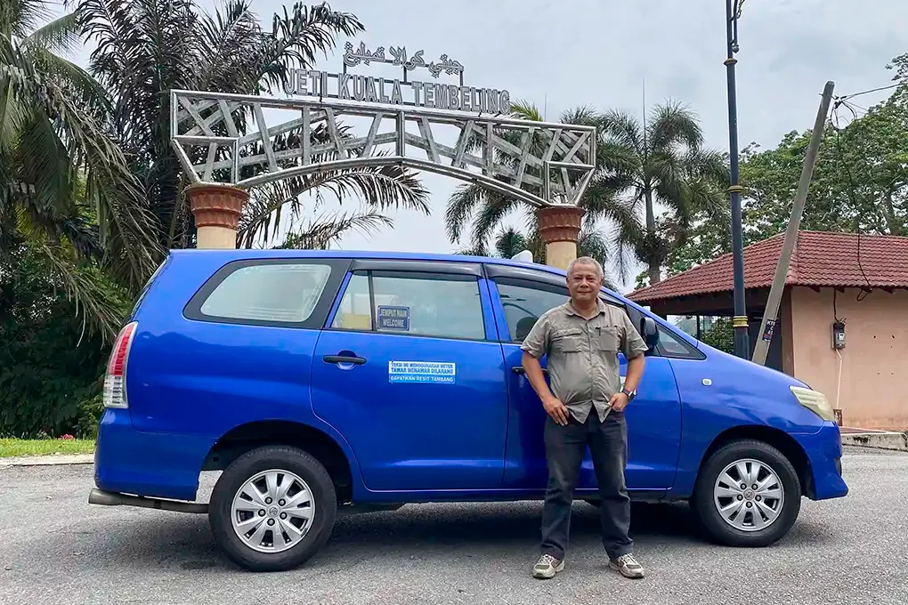 Anuar, a licensed Kuala Lumpur taxi driver, standing next to a Toyota Innova MPV at Jeti Kuala Tembeling jetty, the departure point for Taman Negara transfers.