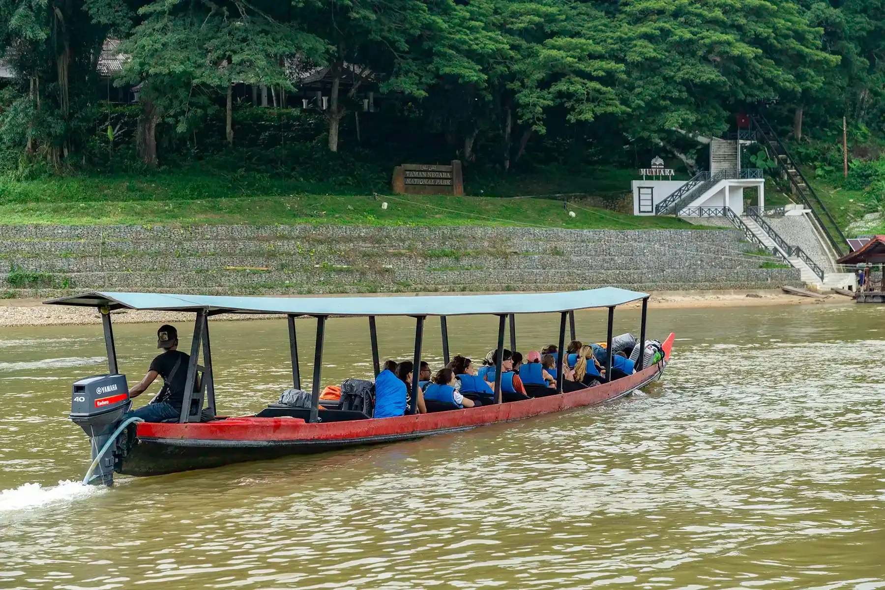 Travellers arriving by traditional longboat at the Kuala Tahan riverside in Taman Negara.