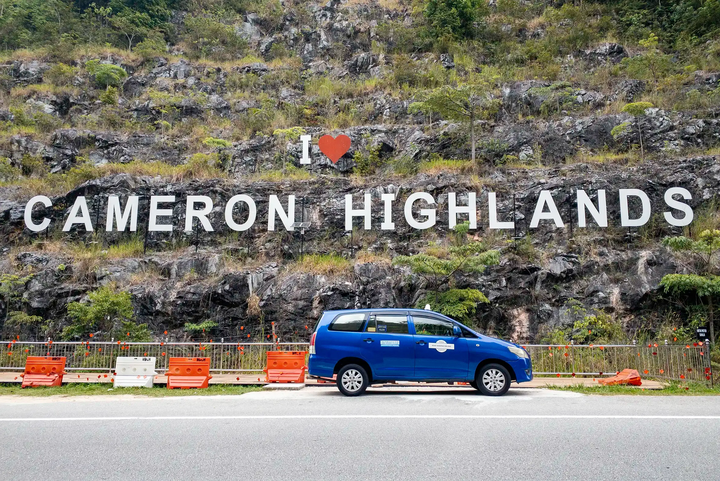 Blue My Little Taxi Toyota Innova parked below the I Love Cameron Highlands hillside sign.